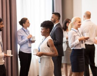 business and education concept - international group of people with conference badges drinking coffee